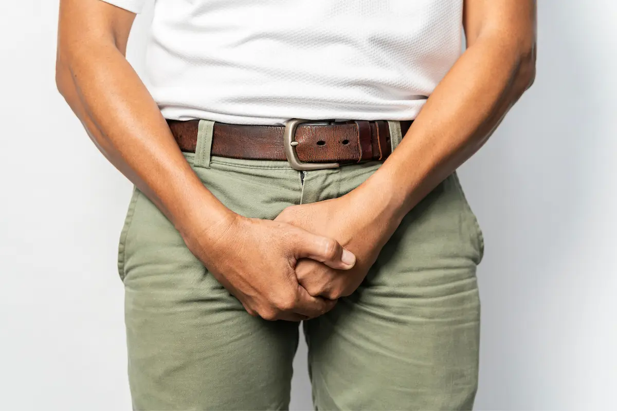 incontinnz-urinaria-uomo Uomo in piedi con le mani posizionate davanti all’area inguinale, gesto che indica un possibile disagio urinario o problema al pavimento pelvico.
